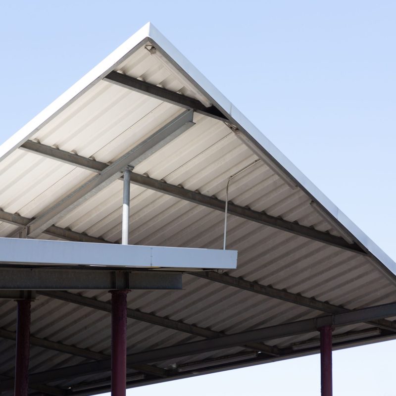 The corner of an old metal roof structure juts up into the blue sky, forming triangles.